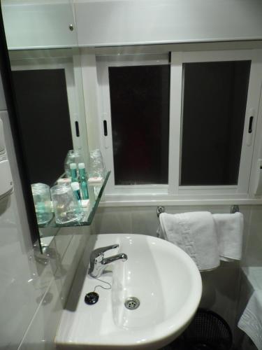 a white sink in a bathroom with two windows at Hostal Arenal in Zaragoza