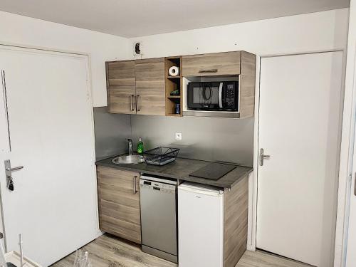 a small kitchen with wooden cabinets and a microwave at 2 PIECES JARDIN, ACCES DIRECT MER ET PROCHE THALASSO in Cabourg