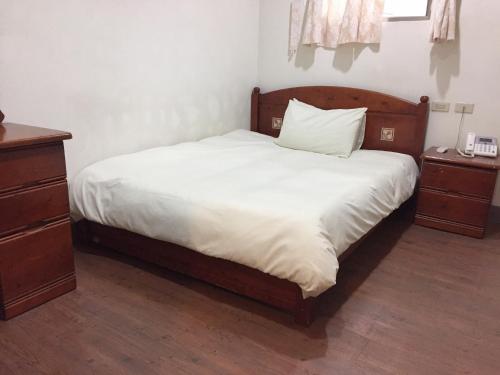 a bed with white sheets and a wooden headboard in a bedroom at Xiang Dou Hotel in Jiaoxi