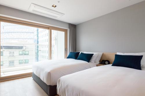 two beds in a room with a large window at Connect Busan Hotel & Residence in Busan