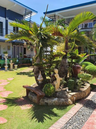 a garden with palm trees and a bench in a yard at L & M Hearthstones Lodge in Oslob