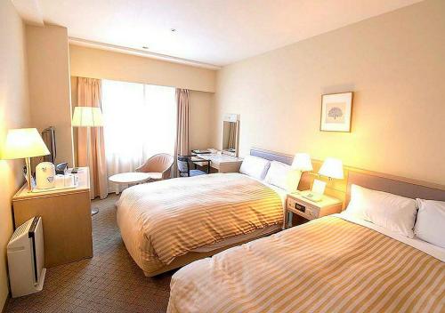 a hotel room with two beds and a desk at Grand Hotel Kanachu Hadano in Hadano