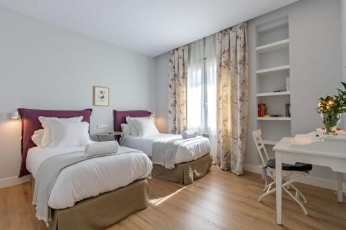 two beds in a room with a desk and a table at Plaza de España Deluxe Suites in Seville