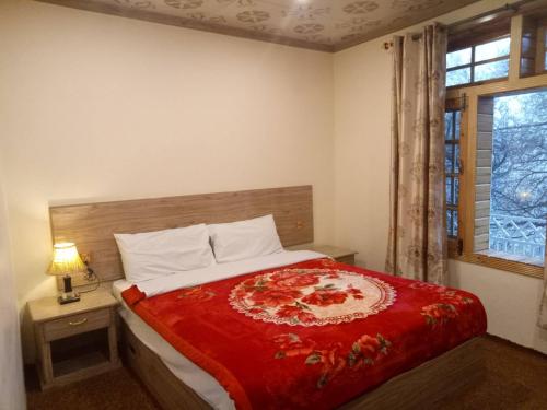 a bedroom with a bed with a red blanket and a window at Hunza Holiday Inn in Baltit