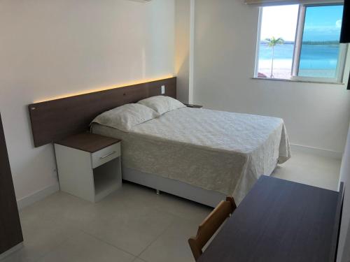 a bedroom with a bed and a table and a window at Apt de frente e com vista Lagoa in Arraial do Cabo