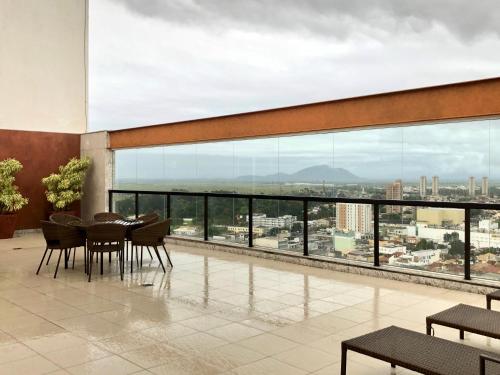 d'un balcon avec une table, des chaises et une grande fenêtre. dans l'établissement Flat pensado para sua tranquilidade e alegria, à Campos dos Goytacazes