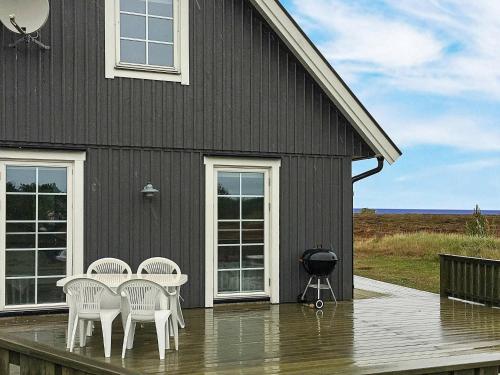 a black house with white chairs and a grill on a deck at 6 person holiday home in L s in Læsø