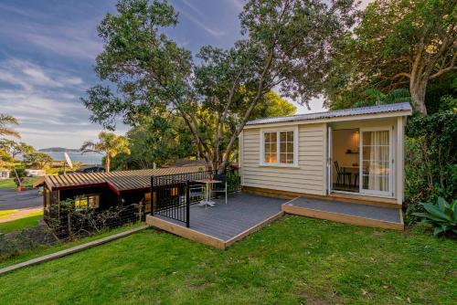 a small white house with a porch and a deck at Anglers Lodge in Coromandel Town