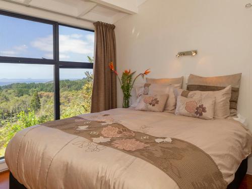 a bedroom with a large bed with a large window at Hahei Hideaway - Hahei Holiday Home in Hahei