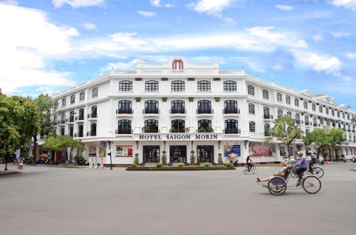 a man riding a bike in front of a white building at Saigon Morin Hotel in Hue