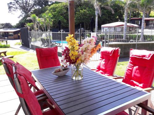 a table with red chairs and a vase of flowers on it at Anglers Lodge in Coromandel Town