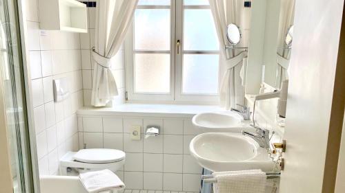 une salle de bains blanche avec deux lavabos et une fenêtre dans l'établissement Hotel Alte Post, à Mindelheim