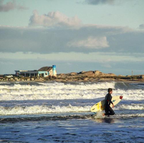 a man walking into the ocean with a surfboard at Cabañas Kundalini Punta del Diablo in Punta Del Diablo