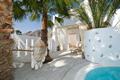 a patio with a hammock and palm trees at Meltemi Village Hotel in Perissa