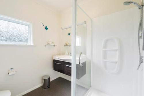 a white bathroom with a shower and a sink at The Green Trout - Paraparaumu Beach Holiday Home in Paraparaumu Beach