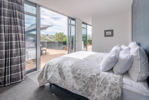 a bedroom with a bed with pillows and a balcony at La Maison De Verre - Akaroa Holiday Home in Akaroa