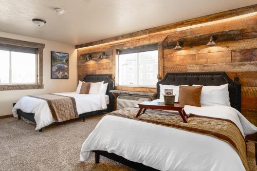 two beds in a room with wooden walls at The Adventure Inn Yellowstone- Jack Creek: 2 Queen Suite 1min from Yellowstone, sleeps 4. in West Yellowstone