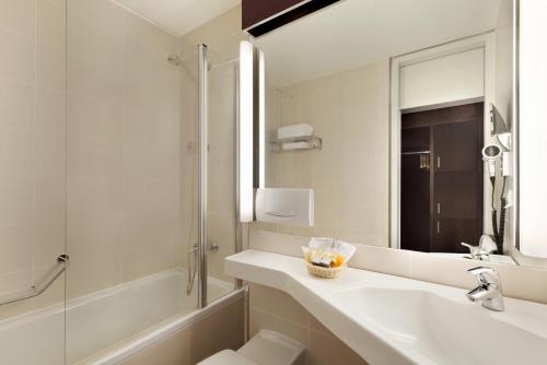 ein Bad mit einem Waschbecken, einer Dusche und einem Spiegel in der Unterkunft Ramada Nürnberg Parkhotel in Nürnberg