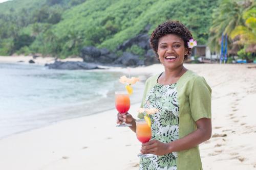 a woman standing on the beach holding a drink at Octopus Resort in Nalauwaki