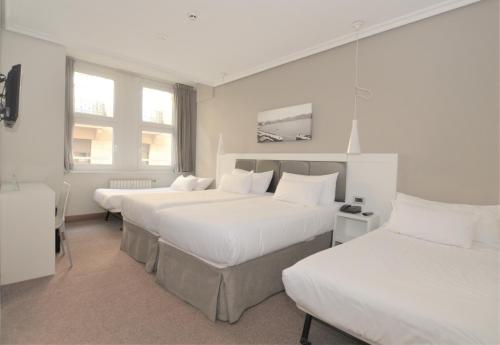 a hotel room with three beds and two windows at Pensión Alemana in Donostia-San Sebastián