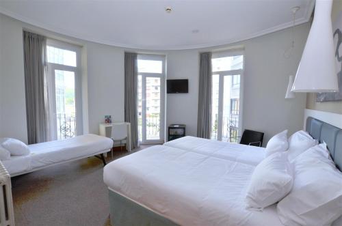 a white bedroom with two beds and windows at Pensión Alemana in Donostia-San Sebastián