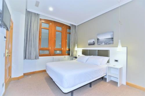 a white bedroom with a white bed and a window at Pensión Alemana in Donostia-San Sebastián