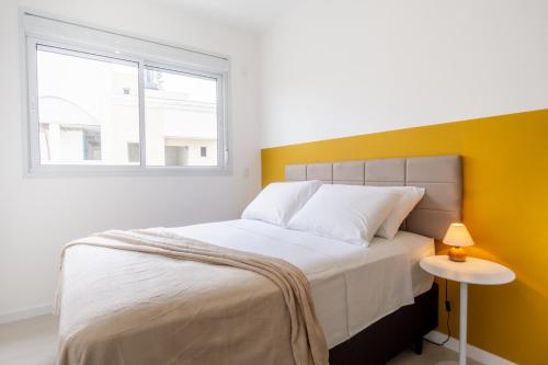 a bedroom with a white bed with a yellow wall at Ambiente Descolado 100m da Praia e Piscina ING4301 in Florianópolis