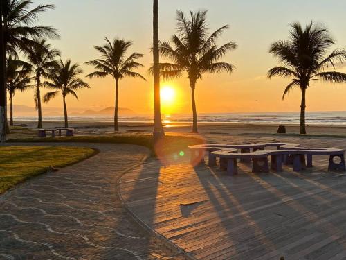 a sunset at the beach with benches and palm trees at Pousada Costa da Riviera PISCINA CLIMATIZADA in Bertioga