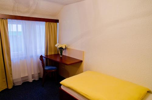 Zimmer mit einem Bett und einem Schreibtisch mit einer Blumenvase in der Unterkunft Hotel Stella in Netphen