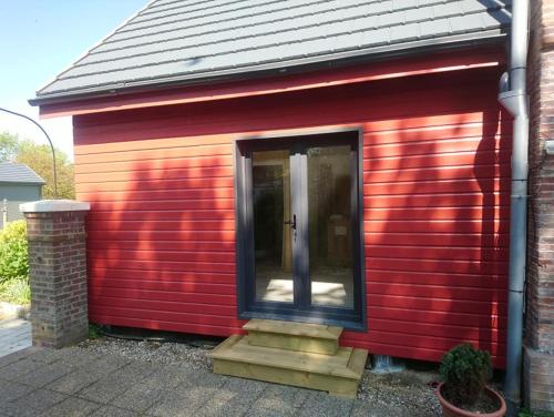 a red shed with a cat sitting in the door at La Nouvelle Criqueboise in Criquebeuf-en-Caux