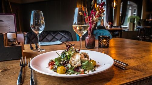 a plate of food on a table with wine glasses at Hotel Café Restaurant 't Raedhûs in Dokkum