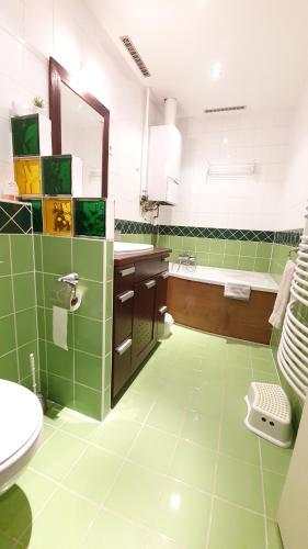 uma casa de banho com azulejos verdes, um lavatório e uma banheira em Deák Apartman em Sopron