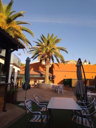 a table and chairs with umbrellas and palm trees at Hospedium Hotel El Nido de Alcudia Suites in Almodóvar del Campo