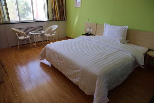 um quarto com uma cama branca, uma mesa e cadeiras em 7Days Inn Hami Baofeng Market em Hami