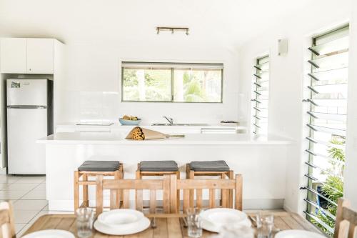 eine weiße Küche mit Holzstühlen und einer Theke in der Unterkunft The Retreat Beach Houses in Peregian Beach
