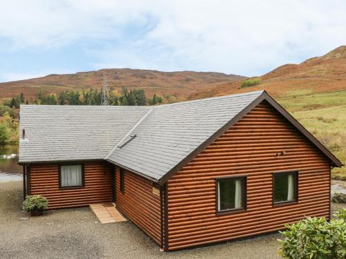 a wooden cabin with mountains in the background at Burnside Lodge Lodge 1, Glengoulandie in Aberfeldy