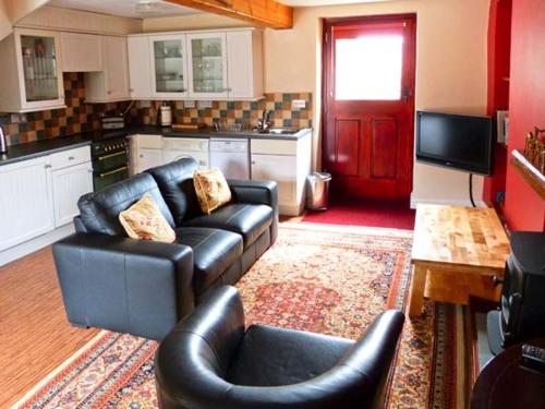 a living room with black leather furniture and a kitchen at The Crook in Great Urswick