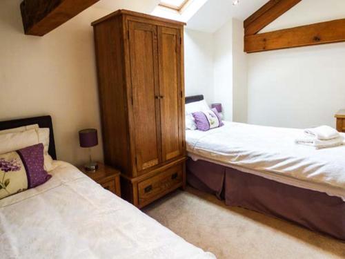 a bedroom with two beds and a wooden cabinet at Ghyll Bank Barn in Staveley