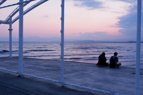 two people sitting on the beach looking at the ocean at IZA Enoshima Guest House and Bar in Fujisawa