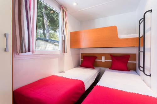 two beds in a small room with red pillows at Camping Village Mare Pineta in Sistiana