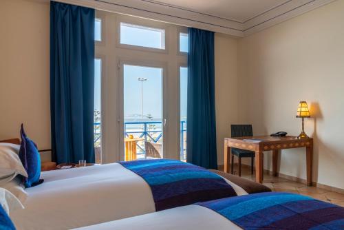 a bedroom with two beds and a desk and a window at Le Médina Essaouira Thalassa Sea & Spa - MGallery Collection in Essaouira