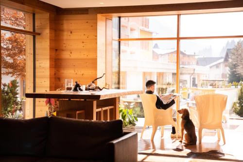 a man sitting in a chair in a living room with a dog at Corona Dolomites Hotel in Andalo