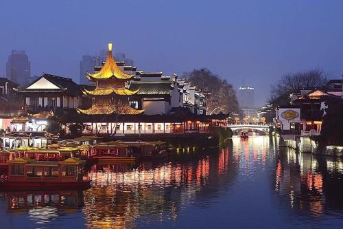 un fiume con un edificio cinese e barche in acqua di 7Days Premium Nanjing Xinjiekou Zhangfu Garden Metro Station a Nanjing