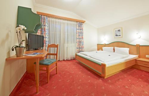 a bedroom with a bed and a desk and a television at HELI'S Bed & Breakfast in Saalbach Hinterglemm