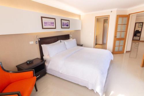 a bedroom with a large white bed and an orange chair at Sonesta Hotel Cali in Cali