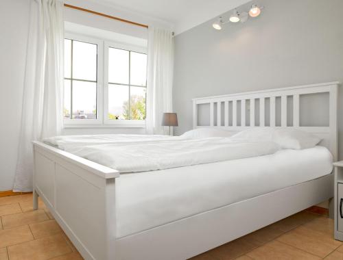 een wit bed in een witte slaapkamer met een raam bij FIP Park Achtern Diek in Insel Poel