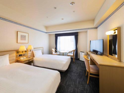 a hotel room with two beds and a desk with a television at Hotel Sapporo Garden Palace in Sapporo