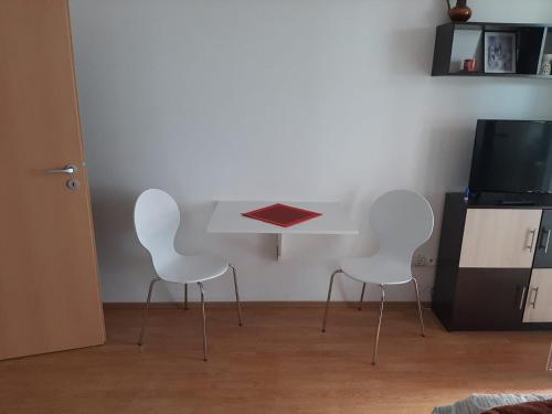 three white chairs in a room with a table and a tv at Apartment Bogdan in Banja Koviljača
