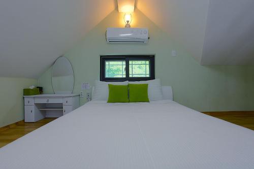 a bedroom with a large white bed with green pillows at Forest of Color Pension in Hongcheon