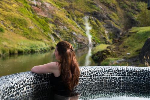 a woman sitting on a wall near a waterfall at Frost and Fire Hotel in Hveragerði